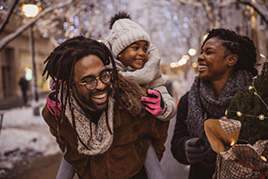 Walking down a snowy street, a black family smiles and embraces in winter